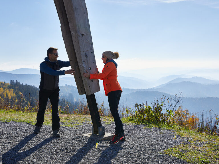 Zwei Personen stehen nach geschafftem Aufstieg lächelnd an einem Pfeiler.