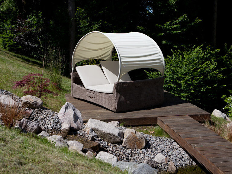 Auf einer Holzplattform steht im Garten des Wellnesshotels eine Doppelliege mit Sonnenüberdachung.