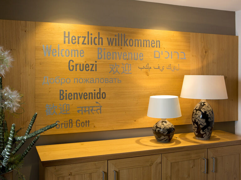 An einer Wand im Waldhotel Grüner Baum im mittleren Schwarzwald ist ein Holzschild auf dem in vielen Sprachen " Herrzlich Wilkommen " steht