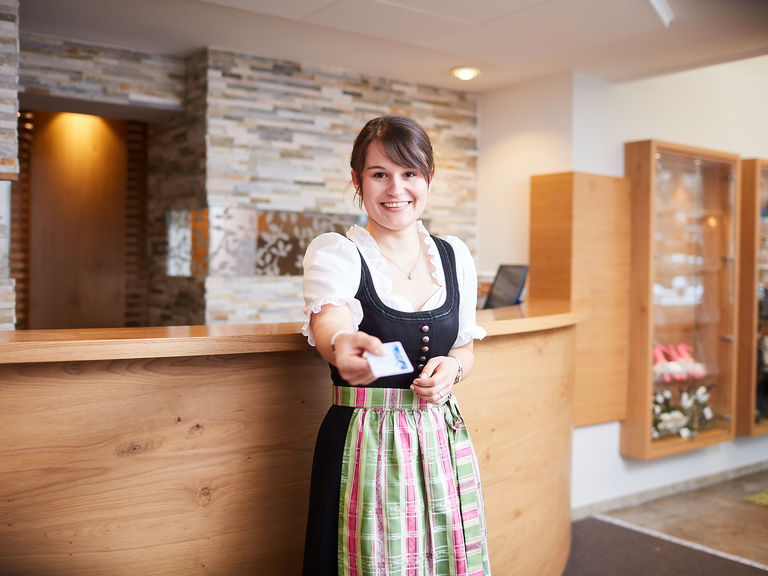 Eine lächelnde Mitarbeiterin des Waldhotels Grüner Baum gibt eine Schlüsselkarte an der Rezeption aus.