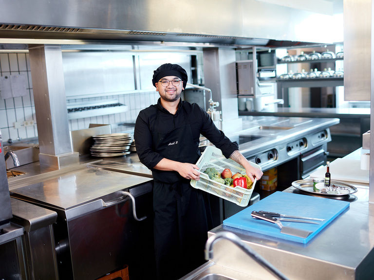 Ein Koch in Uniform hält einen Teller mit Speisen in der modernen Küche des Hotels.