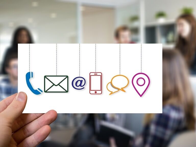 Eine Person hält eine Karte mit verschiedenen Symbolen, wie ein Telefon oder ein Handy in die Höhe.