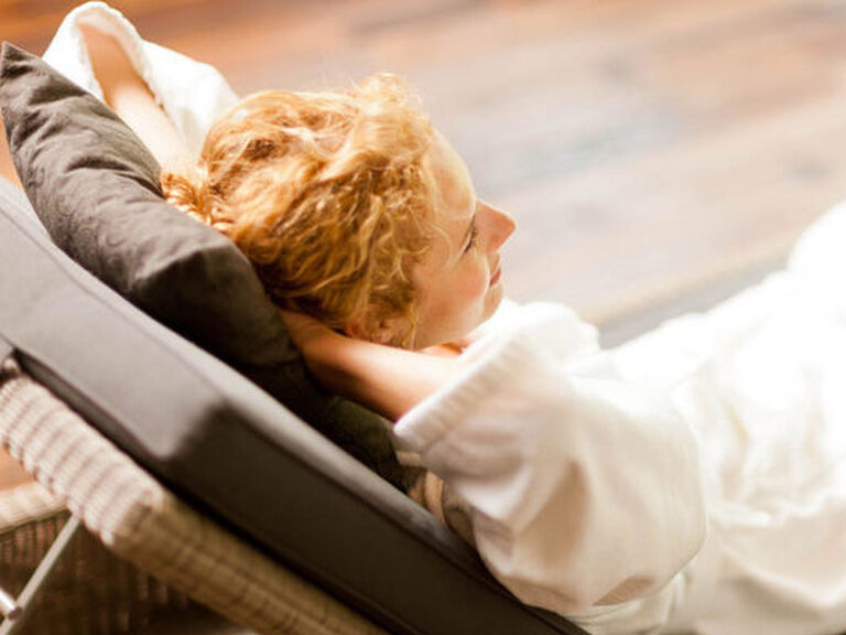 Eine Frau im Bademantel entspannt auf einer gemütlichen Liege und genießt ihren Urlaub im Wellnesshotel.