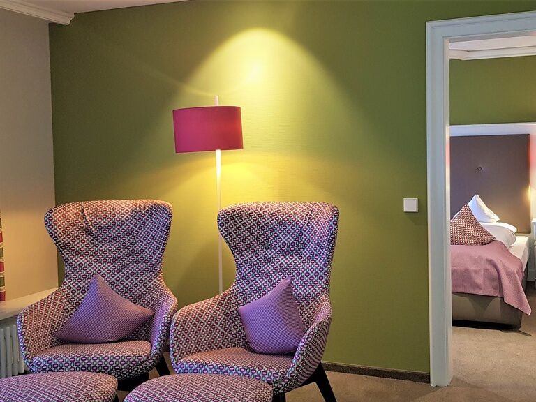 Ein gemütlicher Raum mit zwei Sesseln und dezenter Stehleuchtenbeleuchtung in der Panorama Suite des Waldhotels Grüner Baum im mittleren Schwarzwald.