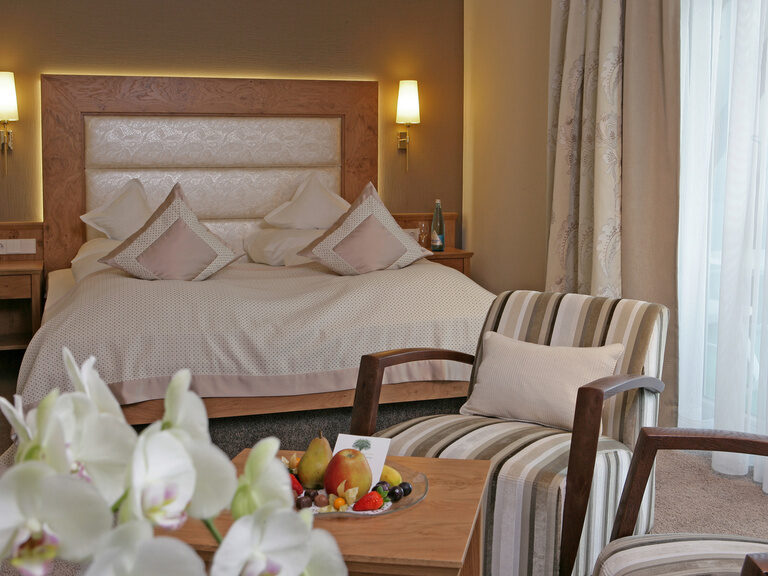 Ein komfortables Schlafzimmer mit einem Tisch voller Blumen neben einem weichen Bett in der Studio Suite des Wellnesshotel Grüner Baum im mittleren Schwarzwald.