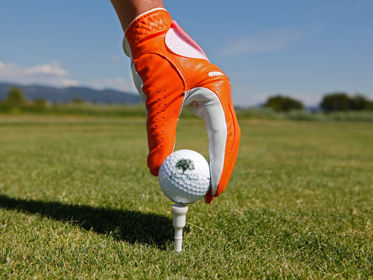 Eine behandschuhte Hand legt einen Golfball auf den Startpunkt eines Holes