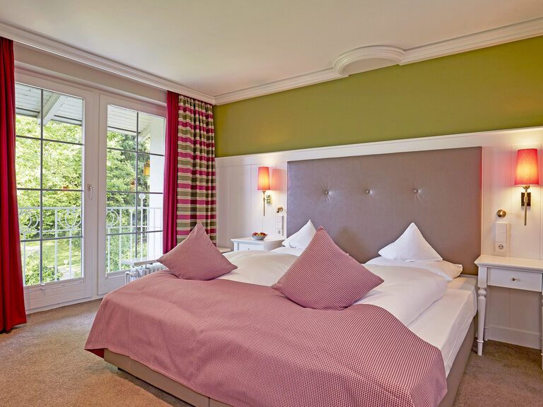 Die Panorama Suite im Wellnesshotel bietet eine schöne Aussicht durch das große Fenster neben dem weichen Bett.