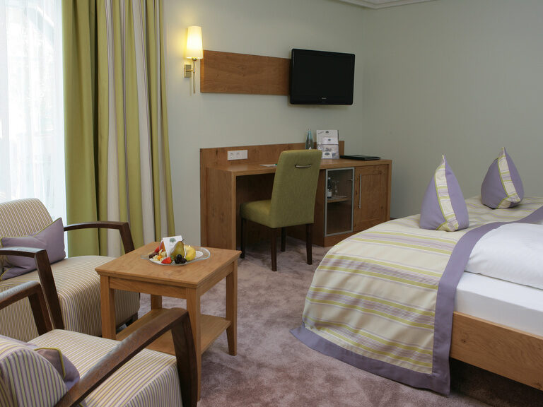 Ein stilvoll eingerichtetes Deluxezimmer mit einem komfortablen Bett, einem eleganten Stuhl und einem modernen Fernseher.