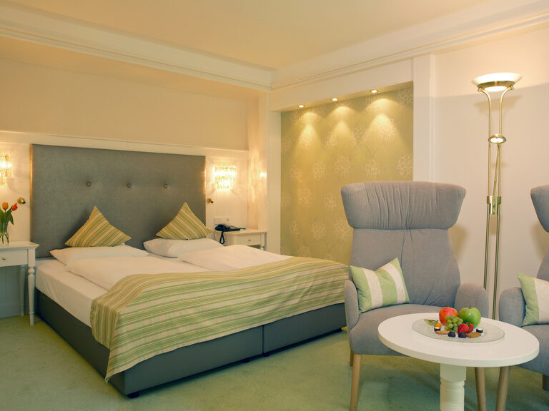 Ein stilvoll eingerichtetes Hotelzimmer mit zwei Stühlen und einem Bett im Waldhotel Grüner Baum im mittleren Schwarzwald.