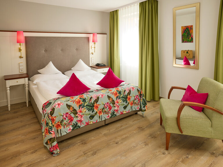 Ein stilvoll eingerichtetes Zimmer mit einem komfortablen Bett einem eleganten Sessel im Wellnesshotel im Schwarzwald.