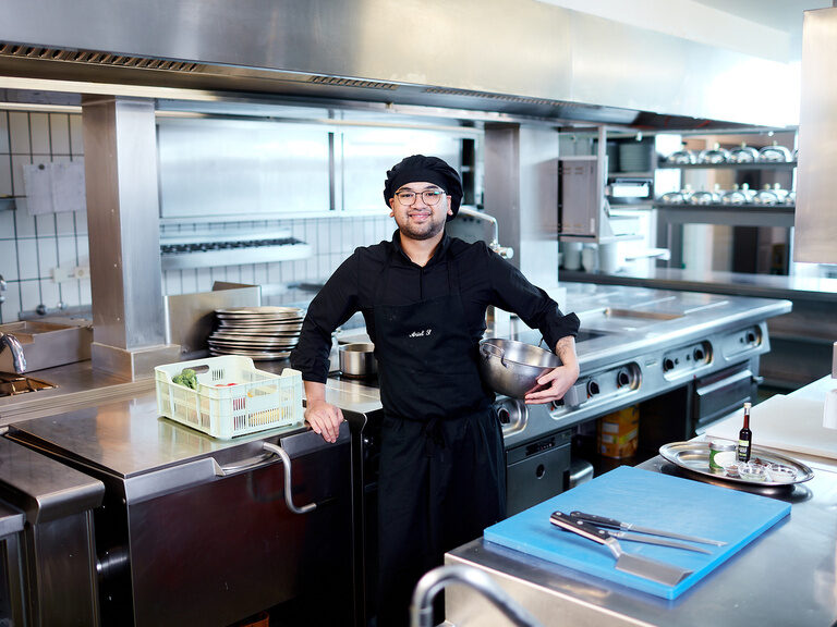 Ein Koch des Waldhotels Grüner Baum lächelt aus der Küche in die Kamera.