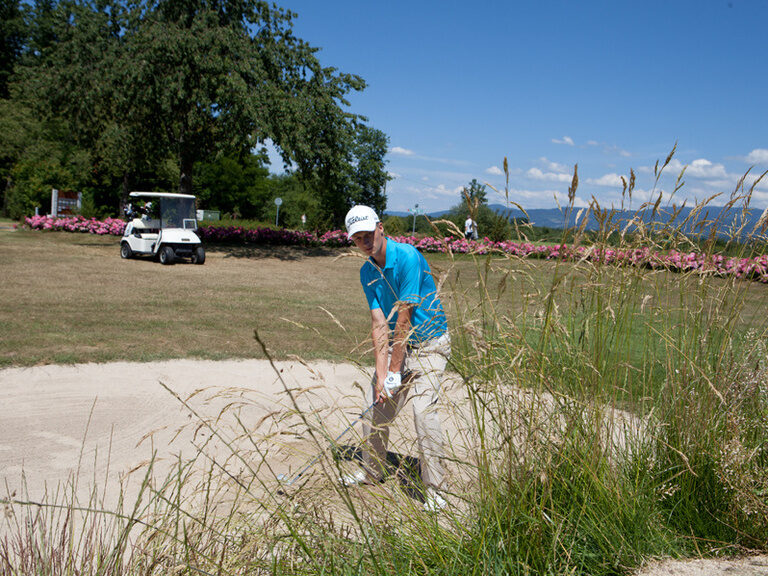 Ein Mann schlägt einen Golfball aus einem mit Sand gefüllten Bunker und probiert das Loch zu treffen.