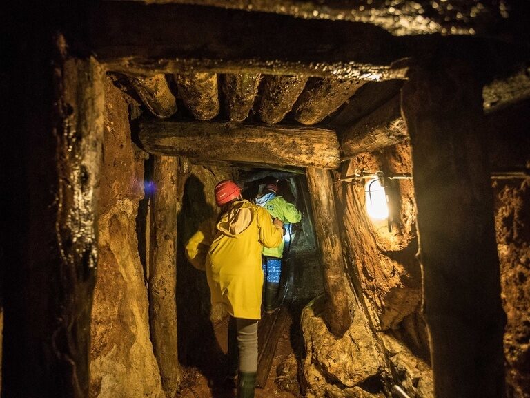 In einem Besucherbergwerk im Schwarzwald erkunden zwei Personen in gelben Mänteln die Stollen.