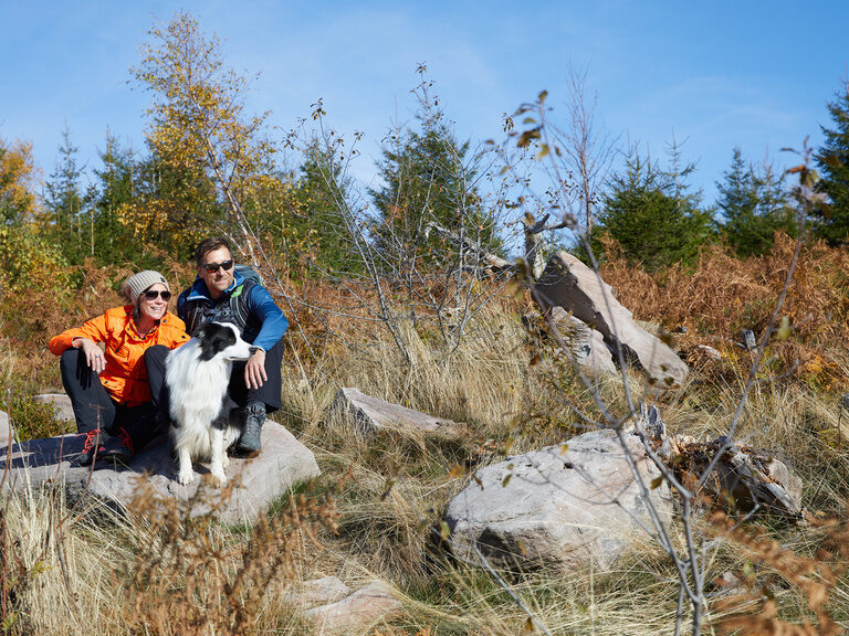 Ein Paar macht beim Wandern mit ihrem Hund eine Pause auf einem Stein.