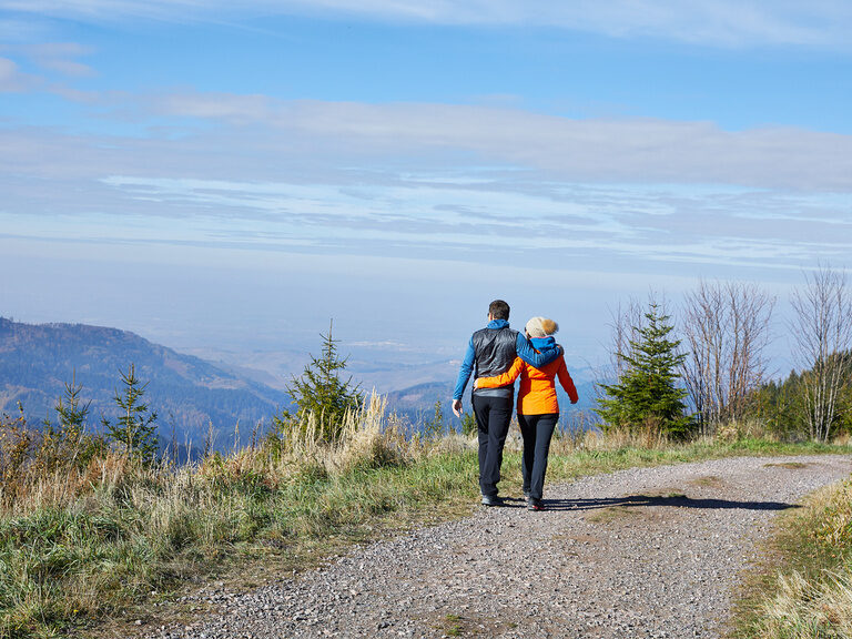 Eine Paar geht auf einem Feldweg spazieren und blickt in die Ferne über den mittleren Schwarzwald