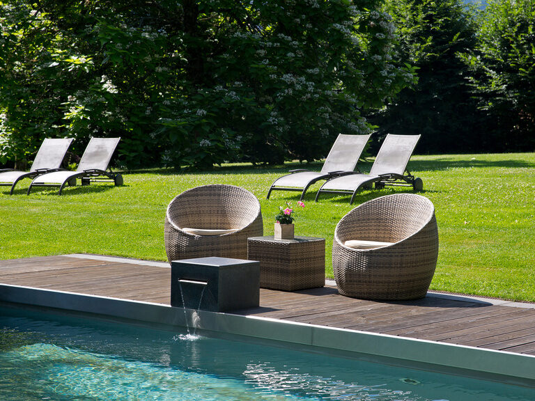 Sitzkörbe stehen am Rand des Aussenpools und im Hintergrund ist die weitläufige Liegewiese zu erkennen.