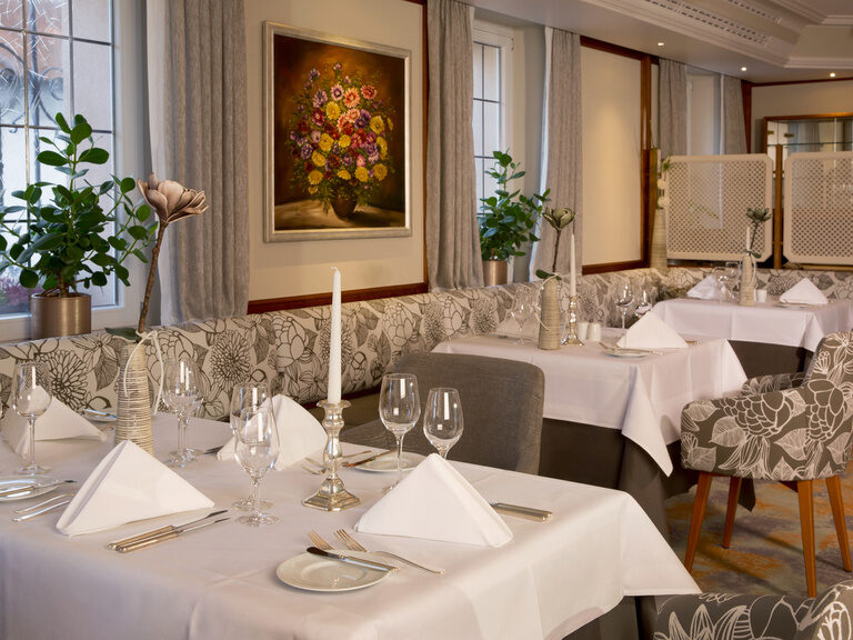 Ein charmantes Restaurant mit weißen Tischdecken, eleganten Stühlen und stilvollen Tischdekorationen im Wellnesshotel.