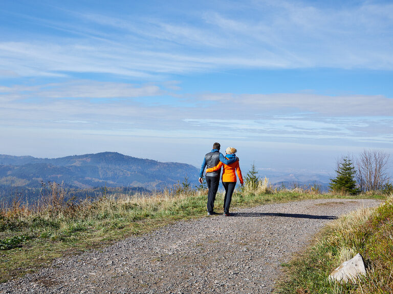 Ein Paar geht beim Wandern auf einem Feldweg und blickt dabei über den mittleren Schwarzwald