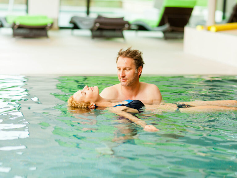 Ein lächelndes Paar genießt die Freizeit im Schwimmbecken des Wellnesshotels Grüner Baum im mittleren Schwarzwald.