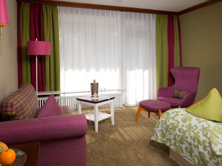 Ein geschmackvoll eingerichtetes Wohnzimmer mit zwei lila Stühlen und einem weißen Couchtisch in einem Zimmer des Wellnesshotels Grüner Baum..